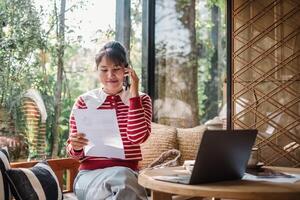 alegre joven mujer multitarea con un negocio llamada y documento análisis en un brillante, lleno de plantas hogar ajuste. foto