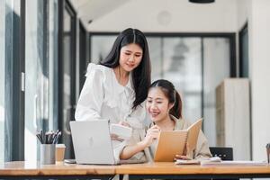 Two focused businesswomen working together, using a laptop and calculator for project planning in a well-lit office. photo