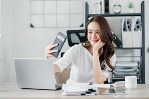 Smiling businesswoman enjoys a light-hearted moment, taking a selfie at her organized office desk with smart phone. photo