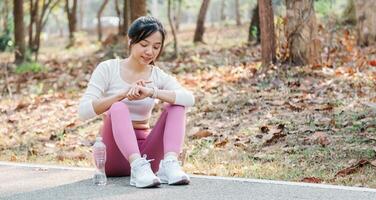 Joyful young woman sitting on a park path, looking at her smartwatch, enjoying a break after a workout session surrounded by nature. photo