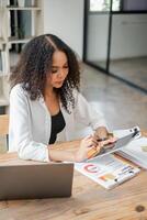 mujer de negocios es absorbido en analizando financiero datos en documentos, con un calculadora y tableta a su espacio de trabajo foto