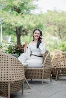 animado persona de libre dedicación teniendo un animado teléfono conversación, cómodamente sentado en un al aire libre patio ajuste con verdor alrededor. foto
