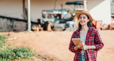 Smiling young farmer holding a notebook stands proudly on her farm with agricultural machinery in the background. photo