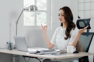 Businesswoman closes her eyes and meditates, practicing mindfulness to maintain balance during a busy workday. photo