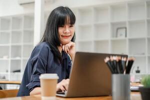 Thoughtful businesswoman in navy blue shirt working on her laptop with a coffee cup and pencils on the desk. photo