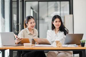 Two focused women in professional attire collaborating on a project with laptops and documents on an office desk. photo