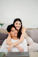 Moment of playful affection is shared as a young woman hugs her partner from behind on the couch, both with joyful expressions. photo