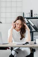 Woman sits at her office desk, massaging her temples in a moment of stress and fatigue amidst a demanding workday. photo