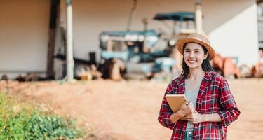 Smiling young farmer holding a notebook stands proudly on her farm with agricultural machinery in the background. photo