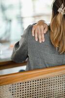 Close-up of an office worker's hand on her shoulder, indicating discomfort or pain, while sitting in an office chair. photo