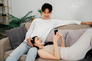 Comfortable Asian couple engages with a smartphone on the sofa, embodying a relaxed and modern home atmosphere. photo