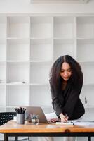 A woman is sitting at a desk with a laptop and a notebook photo