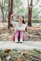 Seated woman in pink leggings takes a selfie with her smartphone in a park filled with fallen leaves and trees. photo