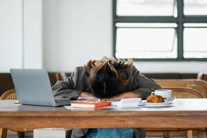 Overworked individual takes a quick nap at their desk, surrounded by a laptop, papers, and a half-eaten breakfast, depicting workplace fatigue. photo