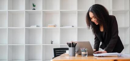 Concentrated businesswoman is busy at work, standing over her desk with documents and a laptop in a modern office setting. photo