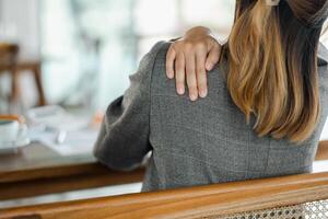 Close-up image captures a person resting their hand on their shoulder, suggesting a break or a moment of discomfort while working at a desk. photo