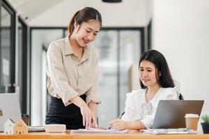 Standing woman with a smile oversees the work of her seated colleague, promoting a collaborative atmosphere in the office. photo