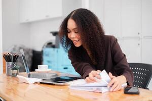 Smiling businesswoman diligently reviewing paper documents at her work desk with a laptop and coffee in the background. photo