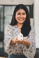 radiante mujer participación fuera un pequeño modelo de un casa, representando propiedad de la vivienda o real inmuebles negocio. foto