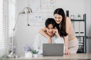 sonriente joven Pareja colabora en un ordenador portátil en un bien organizado hogar oficina espacio, compartiendo ideas y disfrutando cada otros compañía. foto