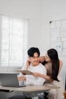 In their light-filled home office, a couple engages in a productive planning session, with the woman leaning over the man as he holds a document. photo