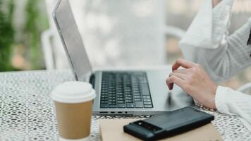 detalle Disparo de un remoto del trabajador manos mecanografía en un ordenador portátil teclado siguiente a un café taza y teléfono inteligente en un al aire libre ajuste. foto