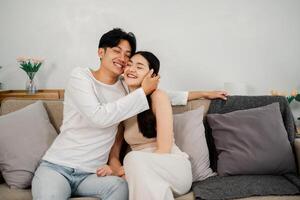 Joyful couple shares a tender moment, laughing and embracing on a cozy sofa in a warmly decorated living room. photo