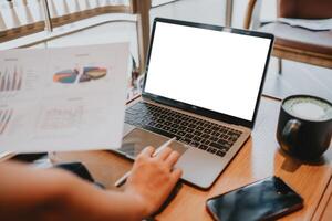 Close-up of a professional's hands working on a laptop with analytical graphs, a smartphone, and a cup of coffee on the table. photo