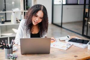 mujer de negocios en oficina atuendo recuento financiero informes en su computadora portátil, indicando completo datos análisis. foto