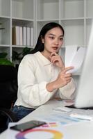 Asian woman freelance graphic designer working with color swatch samples and computer at desk in home office, young lady choosing color gamma for new design project photo