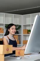 mujer asiático en un en línea Tienda cheque el cliente habla a y paquete información en el ordenador portátil. en línea compras concepto foto