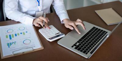 Finance concept. Close up businesswoman hold a graph pen and writing report, and memo, and analyzing business documents with a laptop computer photo