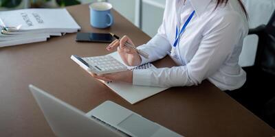 Finance concept. Close up businesswoman hold a graph pen and writing report, and memo, and analyzing business documents with a laptop computer photo