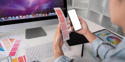 Woman hands holding a smartphone white screen mockup over modern graphic designer office desk photo