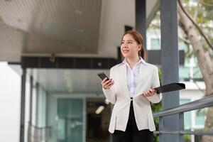 Young Asian business woman entrepreneur, professional manager holding Document file standing on the street in city photo