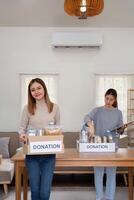 donación y dos mujer voluntario asiático de contento embalaje comida en caja a hogar. caridad foto