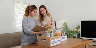 Donation and two woman volunteer asian of happy packing food in box at home. Charity photo