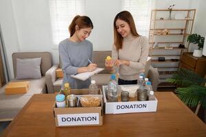 donación y dos mujer voluntario asiático de contento embalaje comida en caja a hogar. caridad foto