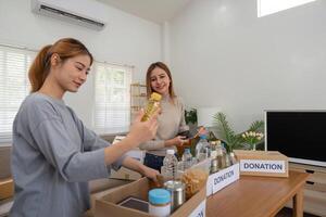 Donation and two woman volunteer asian of happy packing food in box at home. Charity photo