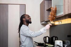 African American man young use duster cleaning in kitchen at home photo