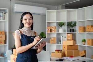 joven negocio mujer asiático trabajando en línea comercio electrónico compras a su tienda. joven mujer vender preparar paquete o empaquetar caja de producto para entregar a cliente. en línea de venta foto