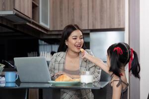 Working mom work from home office. Happy mother and daughter feed snacks to each other. businesswoman and cute child using laptop work freelancer workplace in home, Lifestyle family moment photo