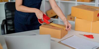 Woman use scotch tape to attach parcel boxes to prepare goods for the process of packaging at home, shipping, online sale internet marketing ecommerce concept startup business idea photo