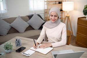 Young muslim business woman calculate budget money finance. Muslim woman accountant use calculator typing laptop counting tax loan bills online payment write document paperwork at home office photo