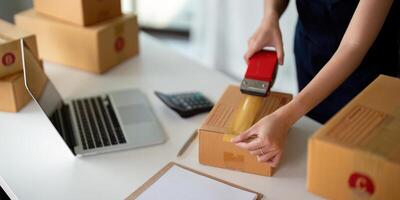 Woman use scotch tape to attach parcel boxes to prepare goods for the process of packaging at home, shipping, online sale internet marketing ecommerce concept startup business idea photo