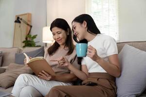 contento mayor madre con adulto hija sentado en sofá y participación tazas con café o té a hogar. disfrutar familia concepto foto