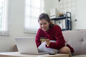 joven asiático mujer manos participación crédito tarjeta y utilizando ordenador portátil para Internet compra. en línea compras, en línea pago a hogar foto