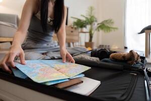 Asian woman packing suitcase or luggage and planning to travel on summer vacation on map photo