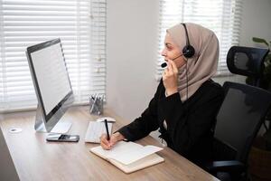 Young muslim women wearing hijab telemarketing or call center agent with headset working on support hotline at office photo