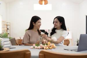 Senior mother and adult daughter happy on the table while arrange flowers in a vase together. Technology and lifestyle concept. Happy time together photo